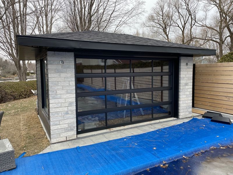 Un garage avec une grande porte vitrée est situé à côté d'une piscine.