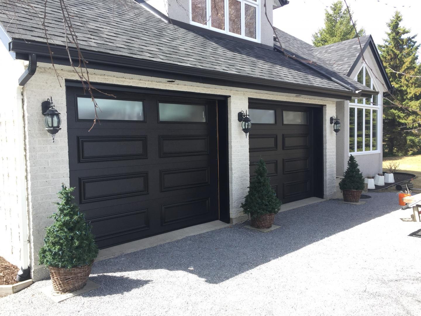 Une grande maison avec deux portes de garage noires et une allée.