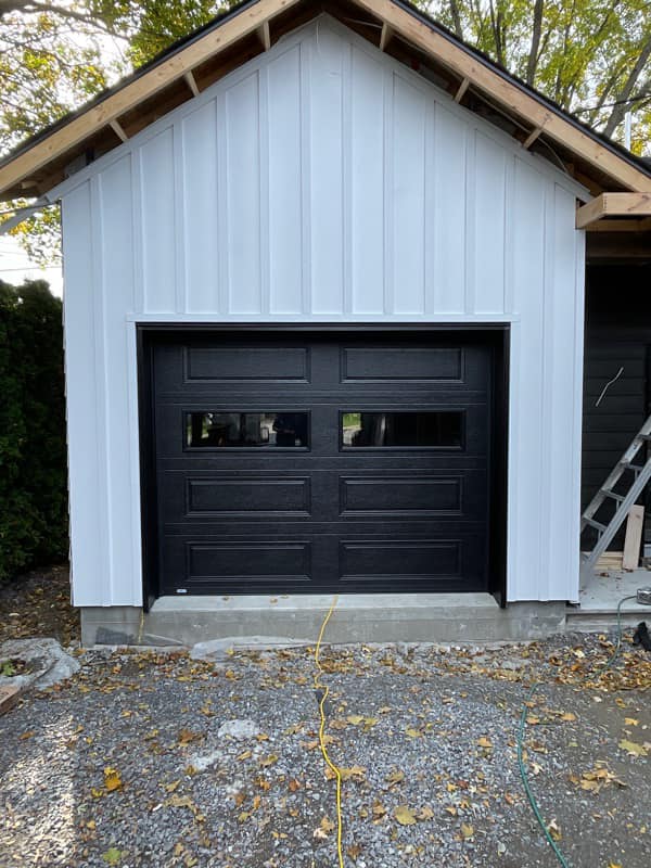 Un garage avec une porte de garage noire et un revêtement blanc.