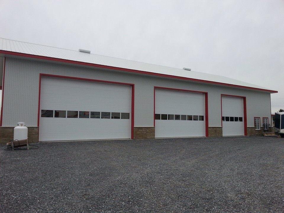 Un grand bâtiment blanc avec trois portes de garage et un réservoir de propane devant.