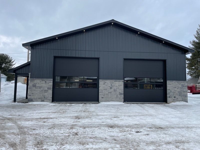 Un grand garage noir avec deux portes de garage dans la neige.