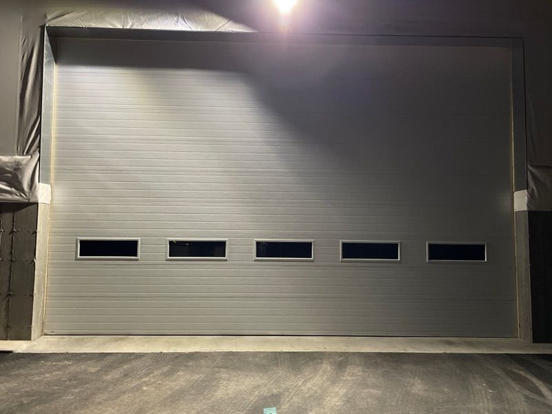 Une grande porte de garage avec beaucoup de fenêtres est éclairée la nuit.