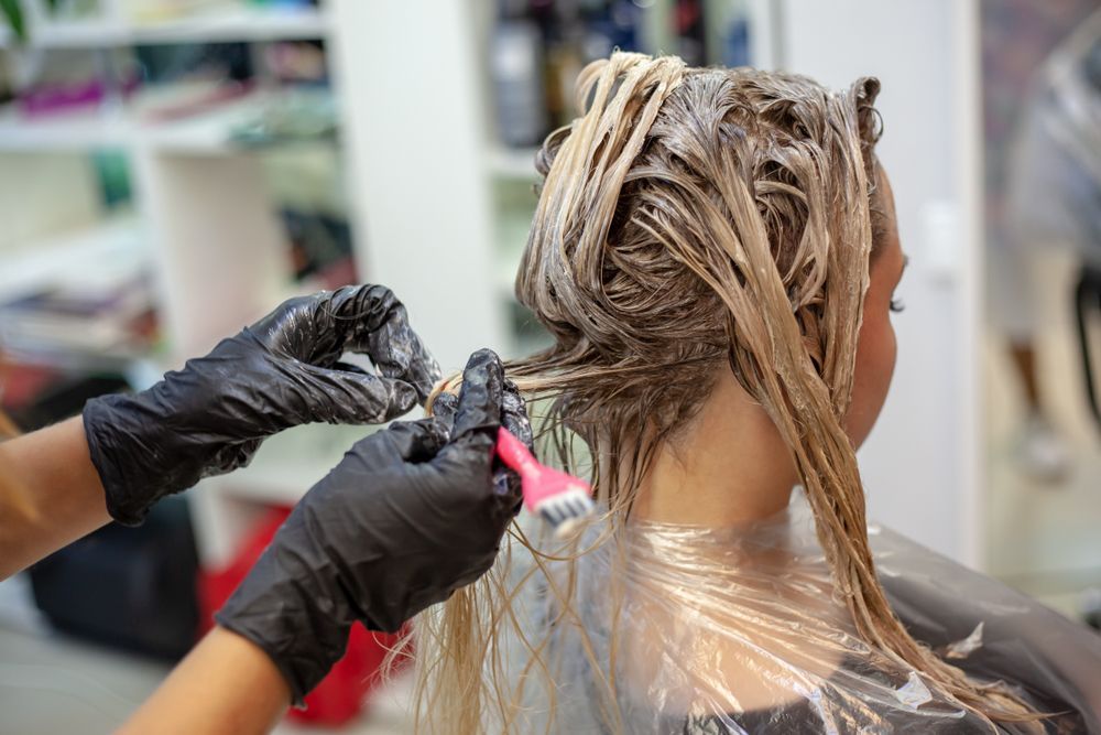 Person getting hair dyed blonde by a gloved hand with a brush. Hair is in foils, in a salon.
