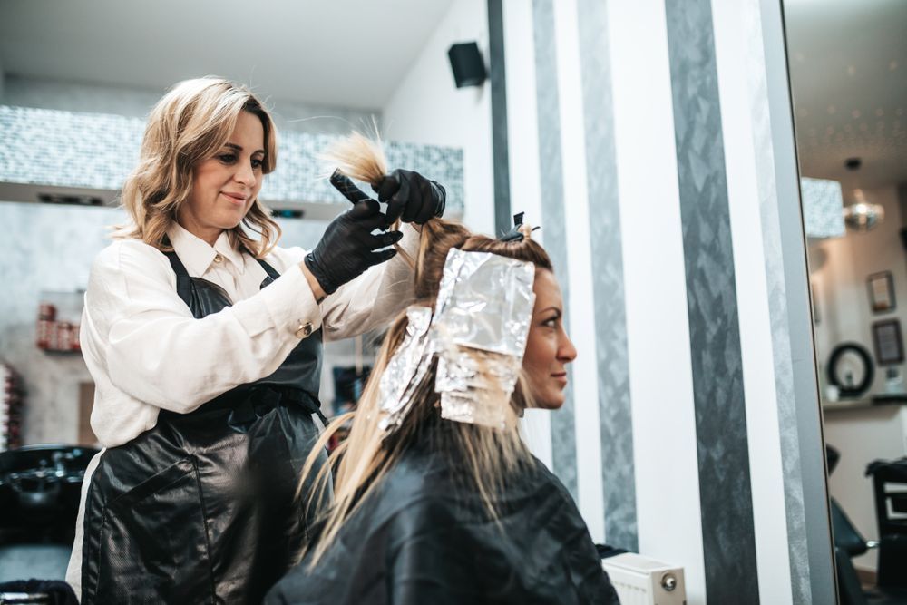 A stylist applies hair dye to a client's hair in a salon.