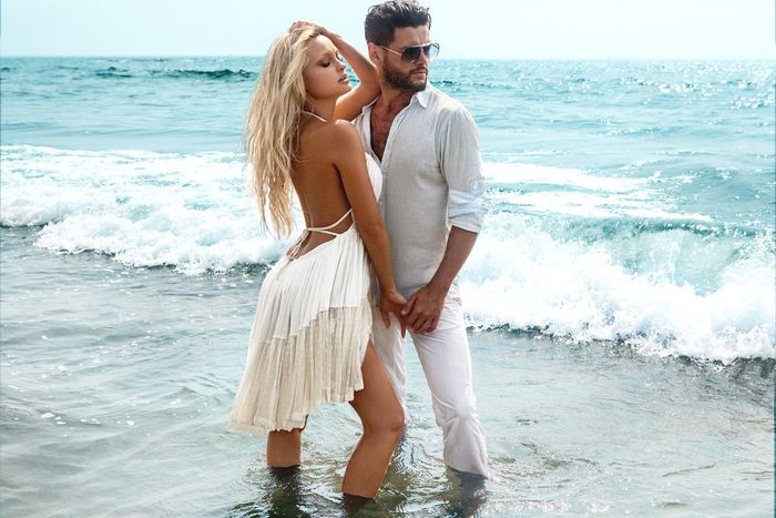 Couple in ocean, woman in white dress, man in white shirt and pants, waves.