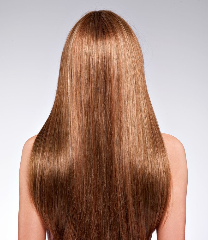 Back view of a person with long, straight, light-brown hair, against a gray background.