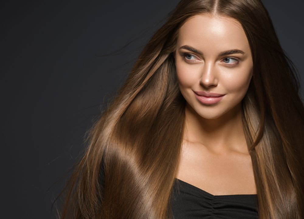 Woman with long, straight brown hair, smiling, against a dark background.