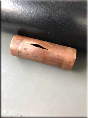 A copper pipe with a hole in it is sitting on a table next to a black pipe.