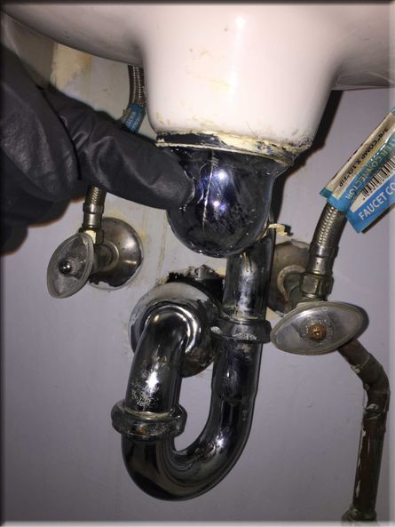 A person wearing black gloves is working on a bathroom sink