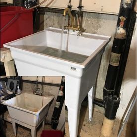 A white laundry sink is sitting in a basement next to a red bucket.