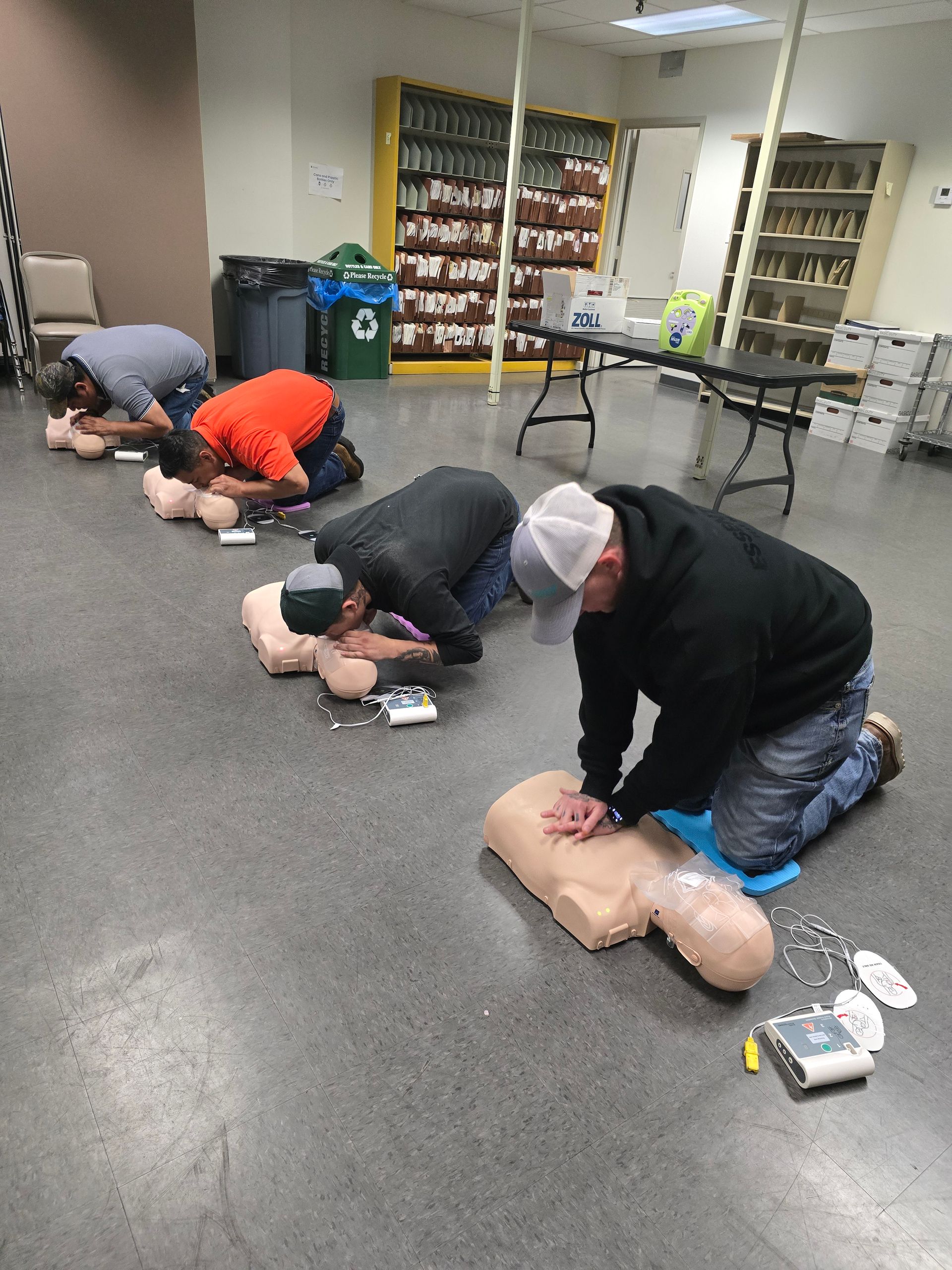 People practicing CPR on mannequins in a classroom.
