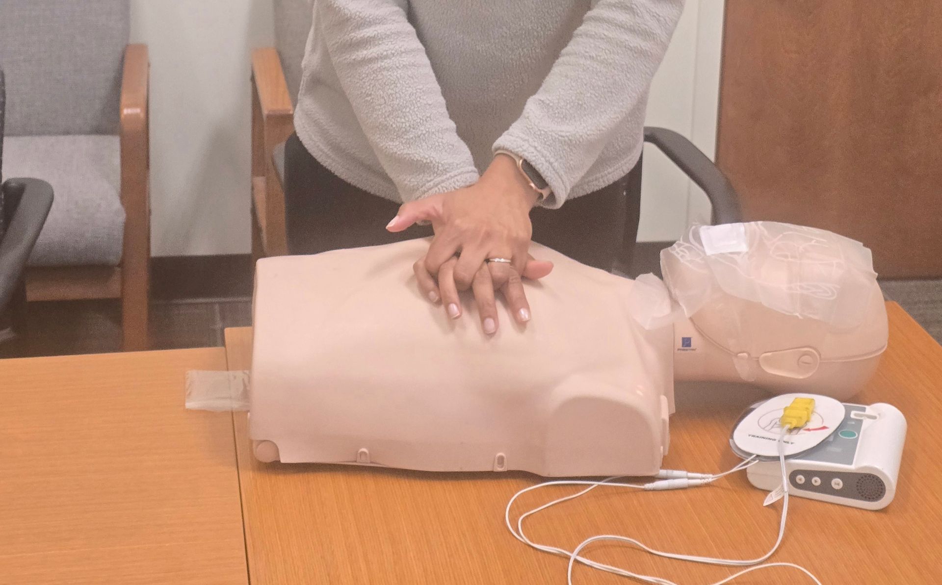 Person demonstrating CPR on a mannequin, with an AED nearby.