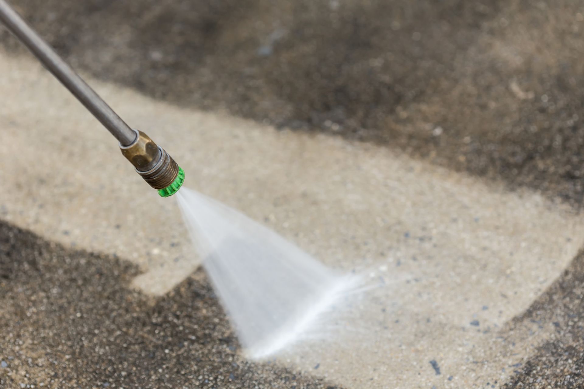 A pressure washer spraying water onto a concrete surface, creating a clean, light-colored path.