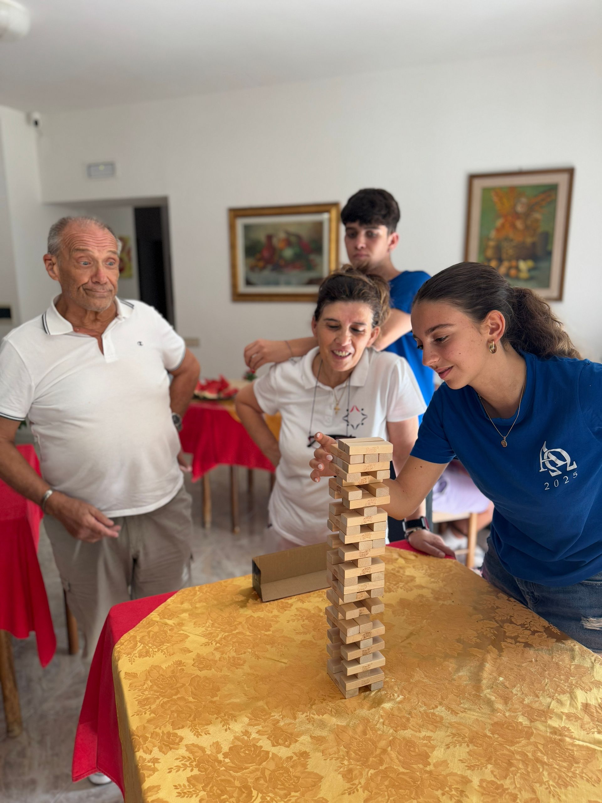 Quattro persone erano riunite attorno a un tavolo per giocare a Jenga in una stanza con quadri incorniciati alle pareti.