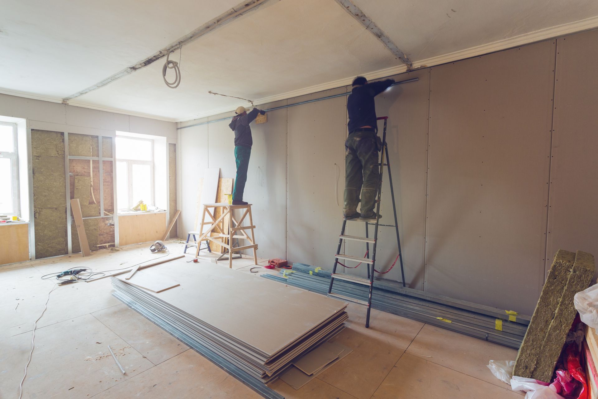 Skilled workers carefully installing plasterboard (drywall) on gypsum walls inside an apartment that is currently under construction.