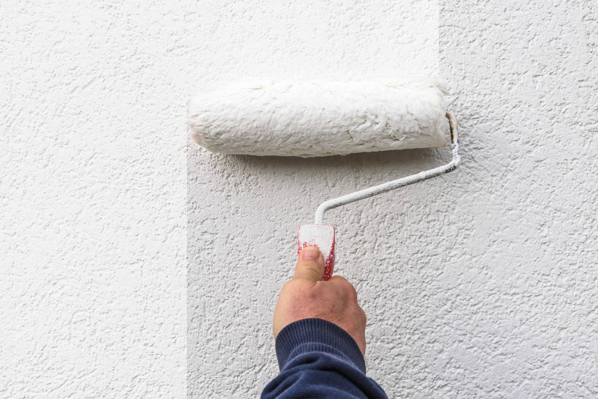 A hand gripping a paint roller as it applies a fresh coat of paint to a wall.