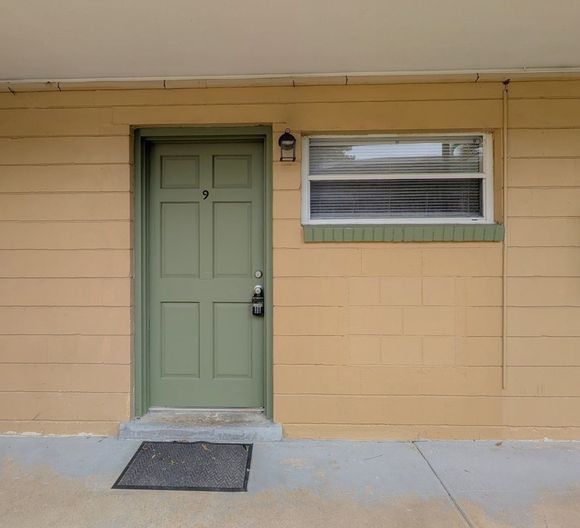 Green door with number 9, next to a window, on a yellow-painted building exterior.