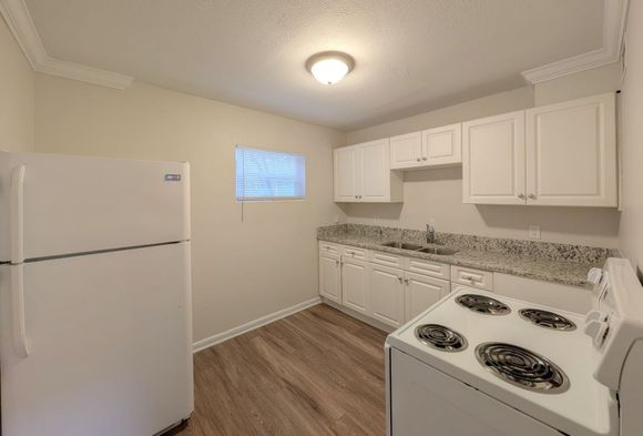 White kitchen with refrigerator, cabinets, granite countertops, and stove.