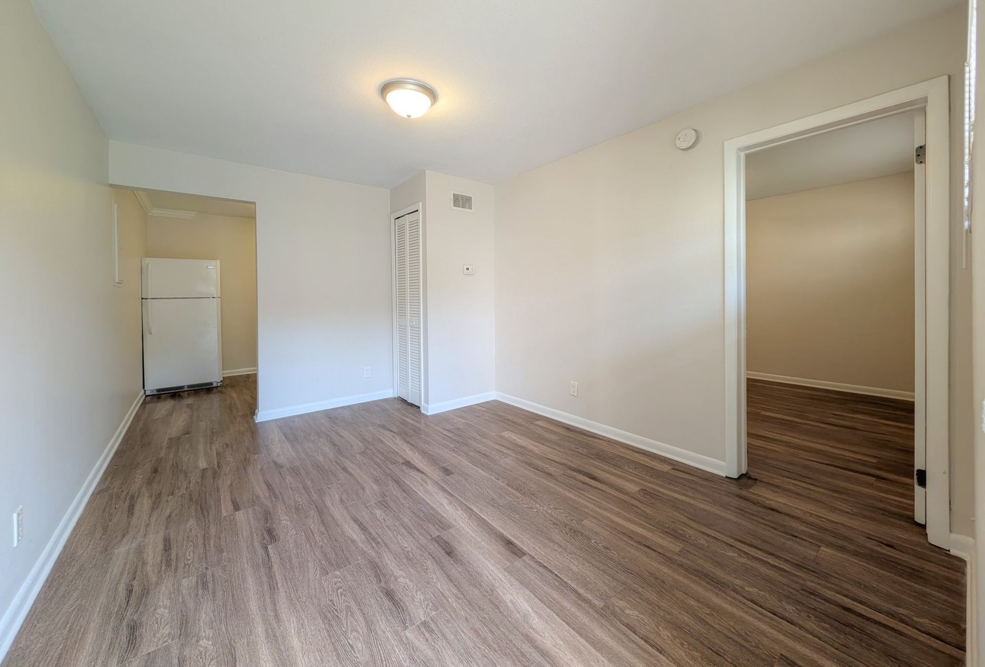 Empty room with wood-look flooring, white walls, and doorways leading to other rooms.