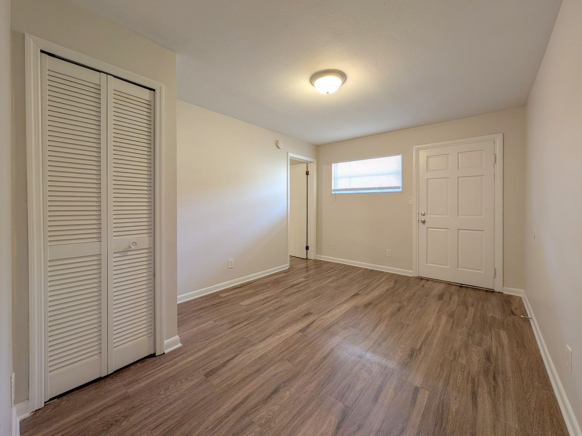 Empty room with wood-look flooring, white walls, closet, doors, and a small window.