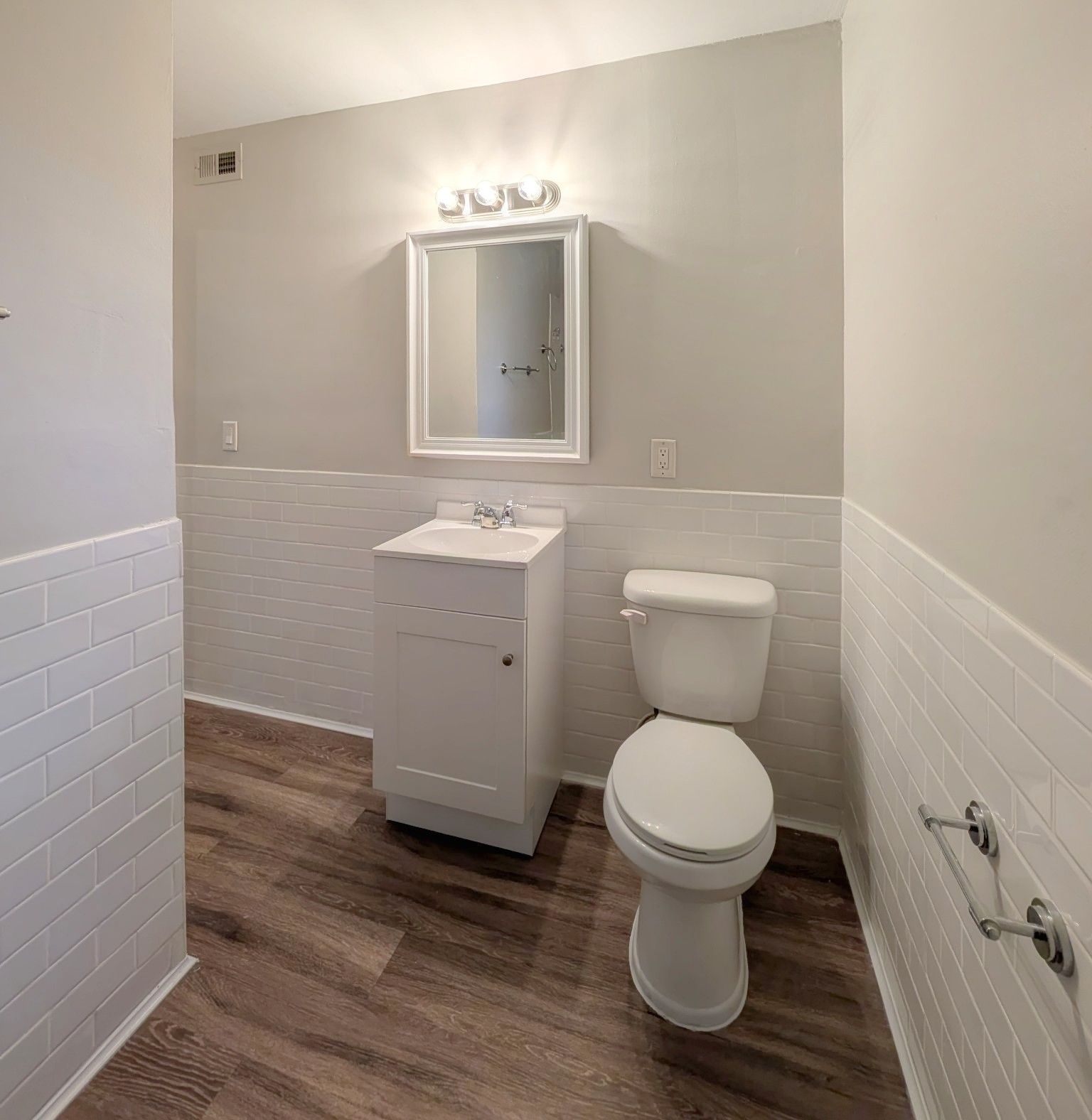Bathroom with white walls and fixtures, wood-look floor, and a mirror above the sink.