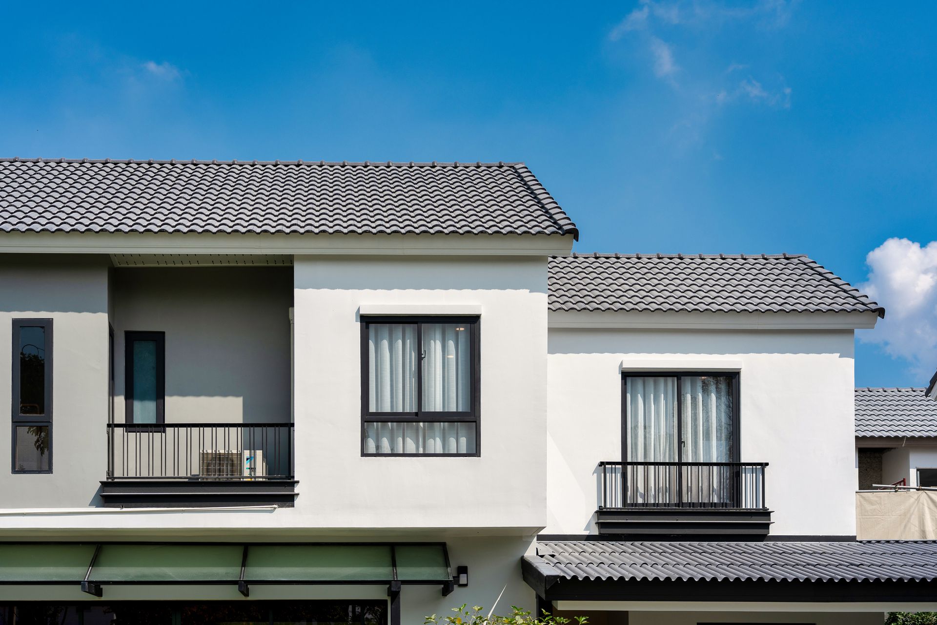 White building with dark framed windows and gray tile roof under a blue sky.