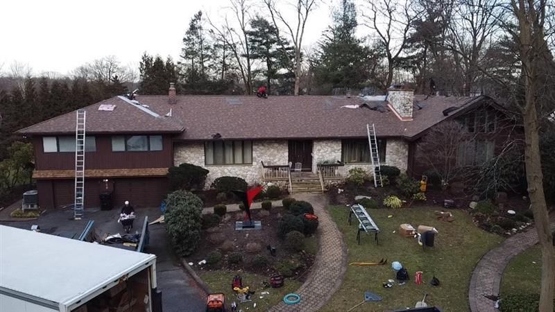 Man on a roof working, with a ladder and scaffolding next to brick building with window.