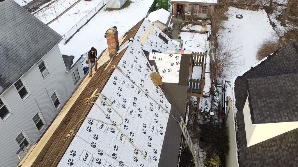 Yellow house with gray shingled roof, blue sky backdrop.