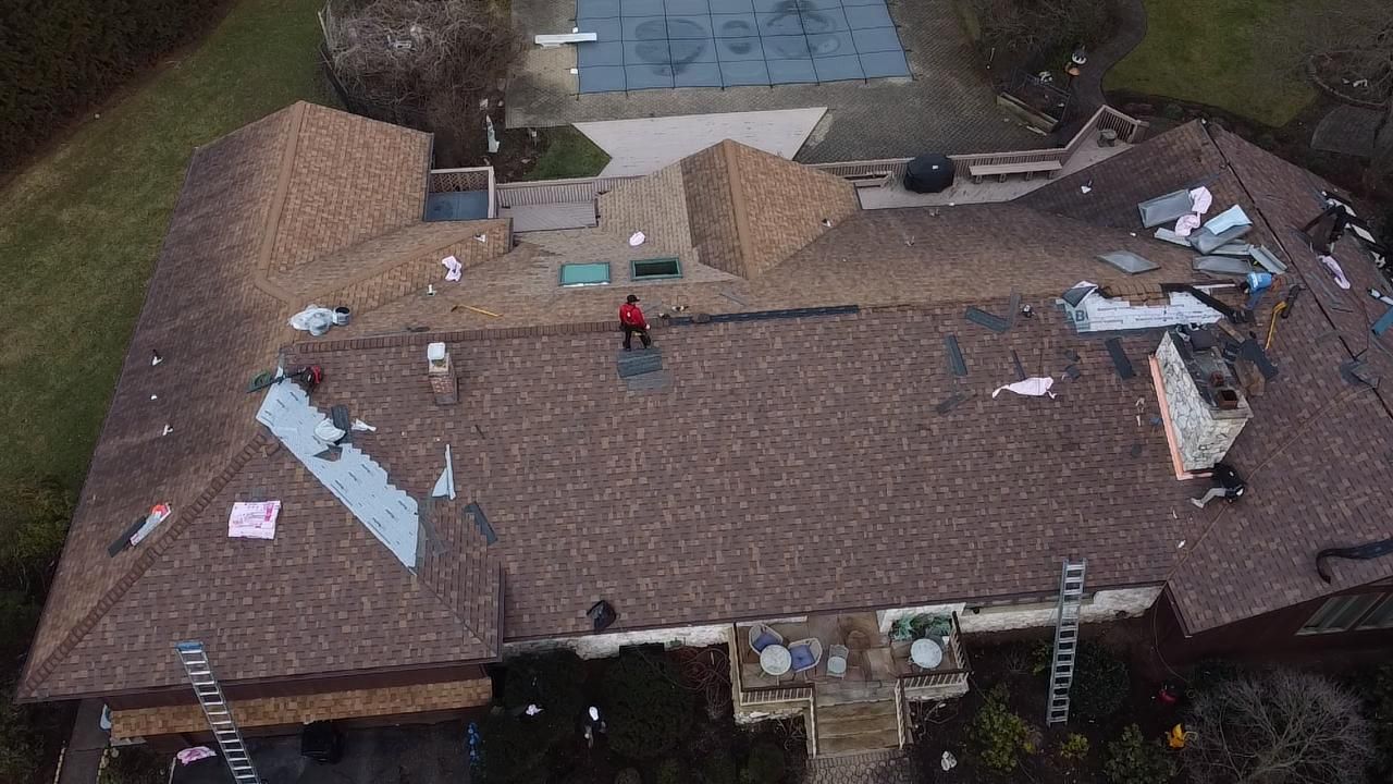 An aerial view of workers on a residential roof during a repair project, with ladders and construction materials present.