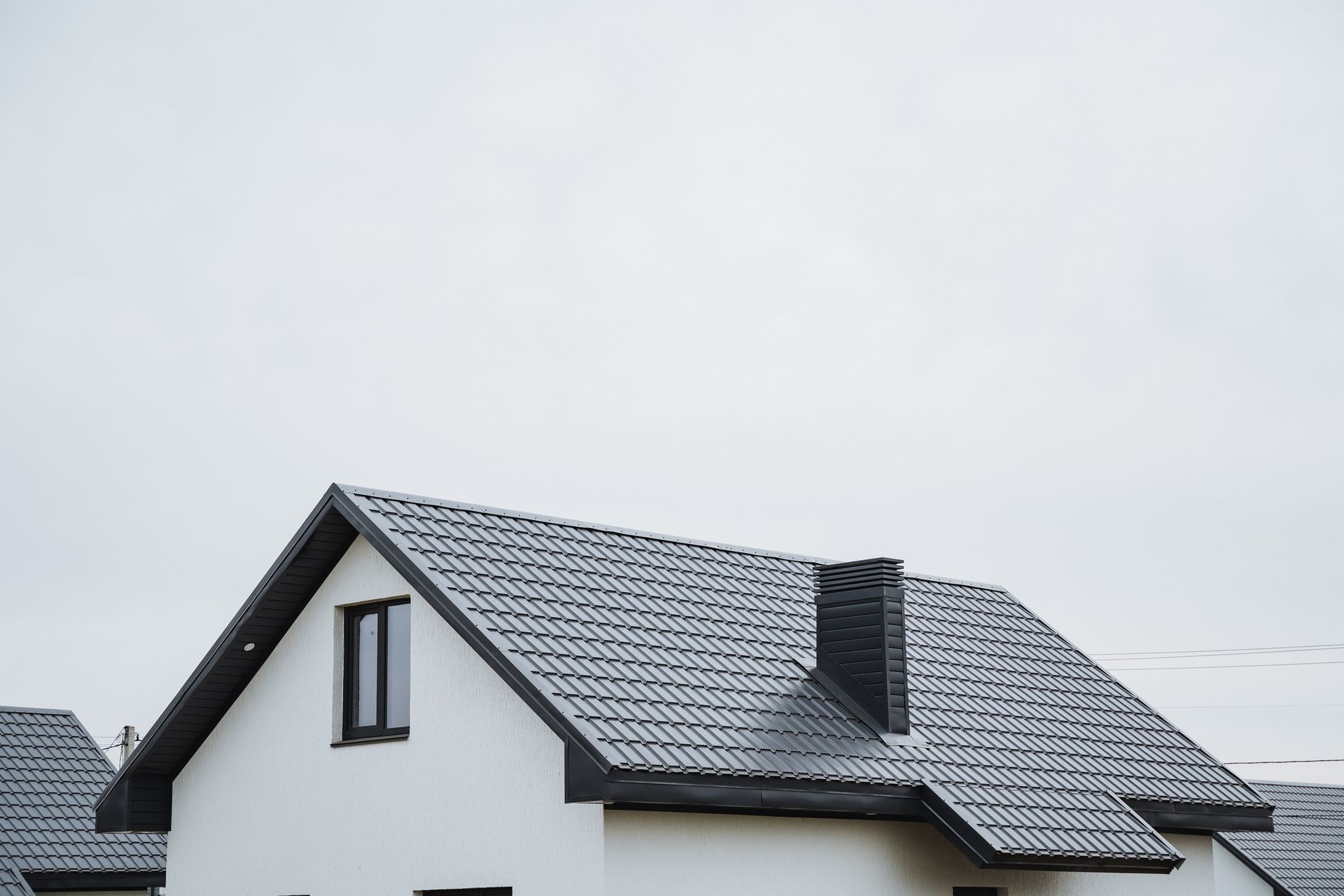 White house with dark gray roof and chimney against a cloudy sky.