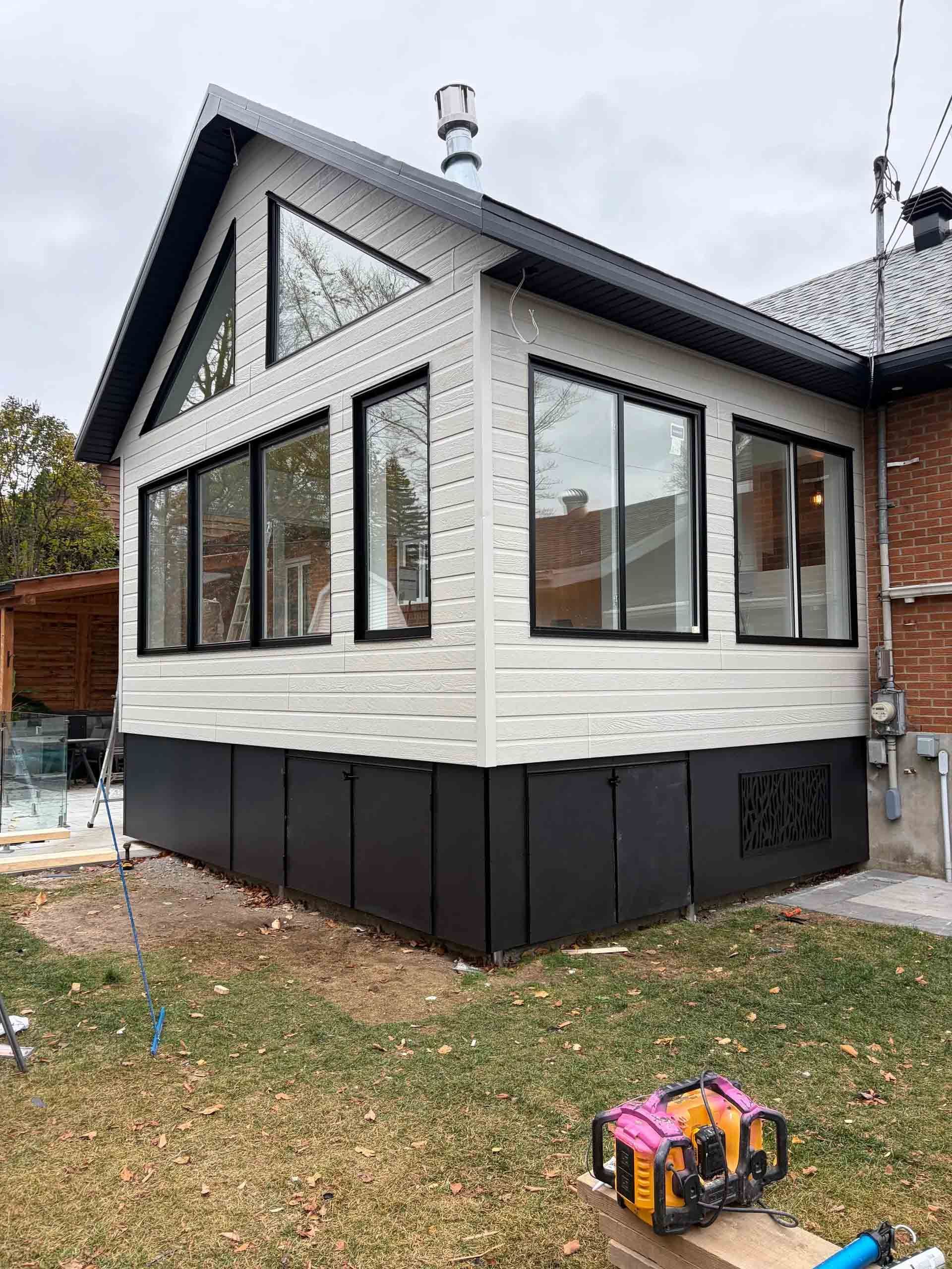 Véranda neuve avec bardage noir et blanc et grandes fenêtres, attenante à une maison en briques.