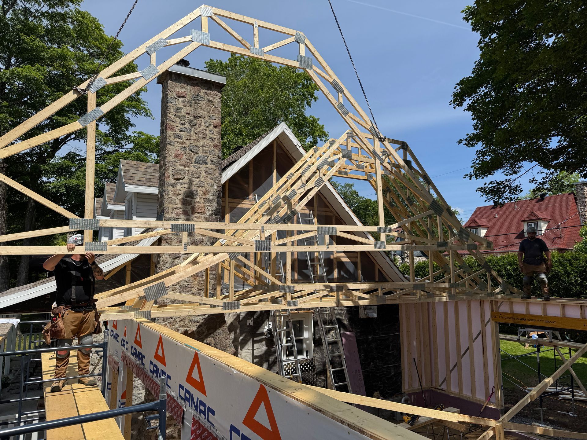 Des ouvriers du bâtiment installent une charpente en bois sur une maison avec une cheminée en pierre.