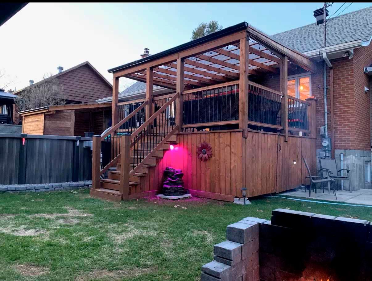 Terrasse en bois avec pergola, escalier et éclairage rose dans un jardin.