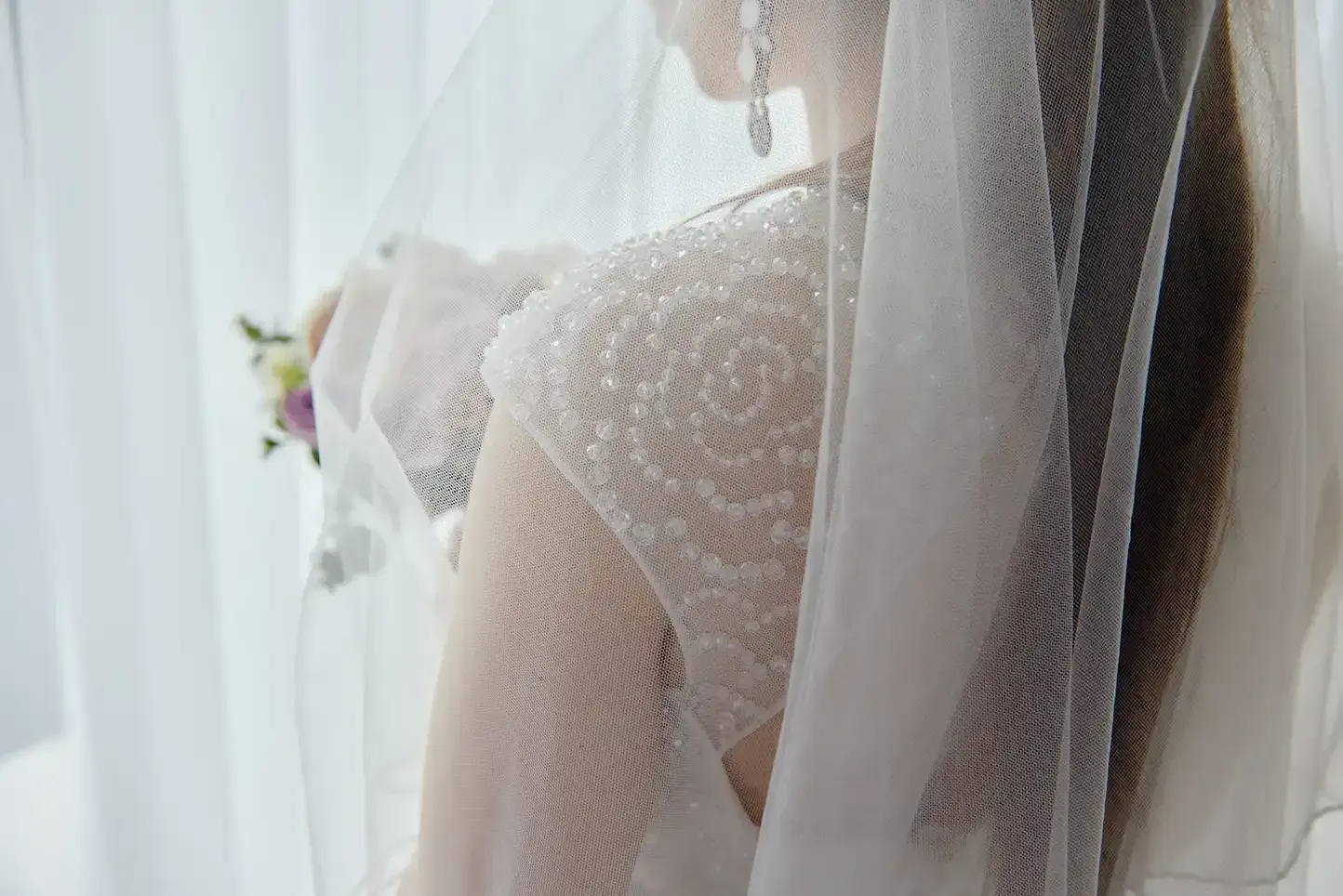A bride in a wedding dress and veil is standing in front of a window.