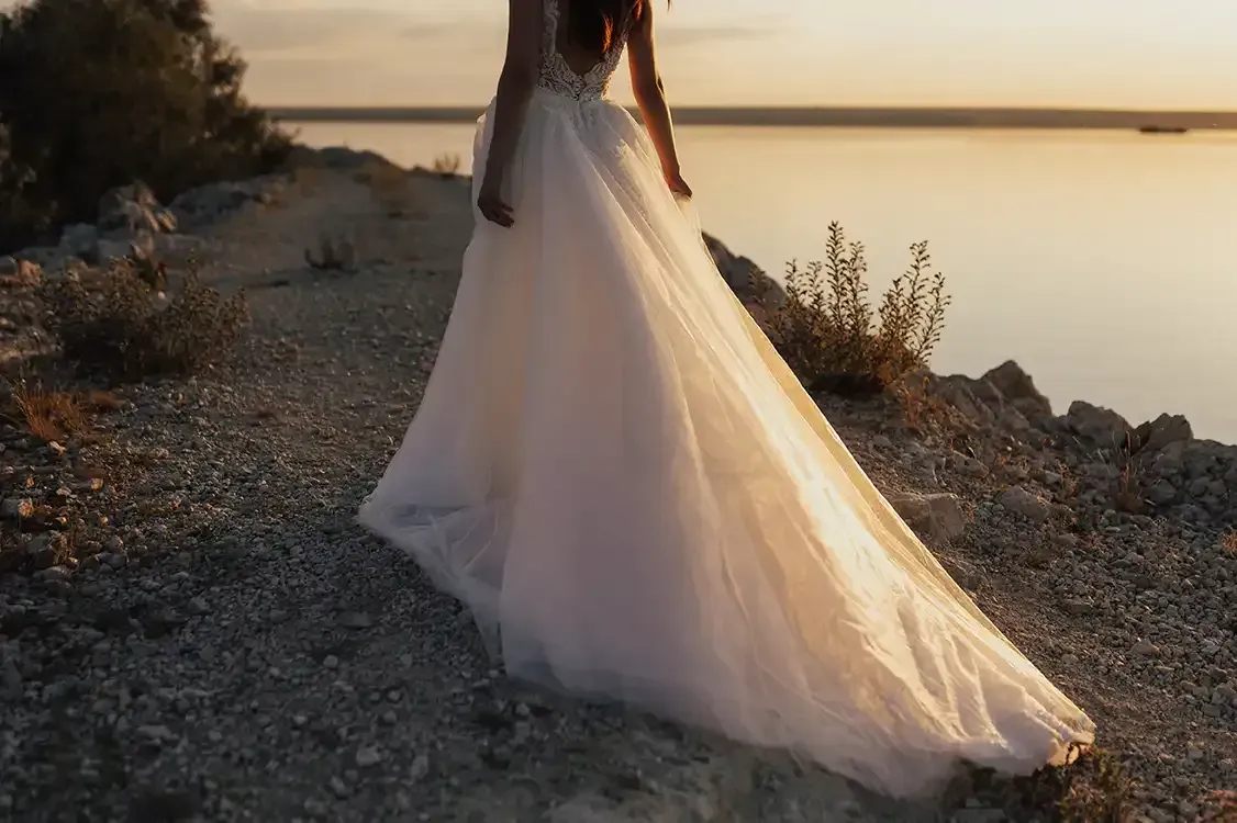 A woman in a wedding dress is standing on the shore of a lake.