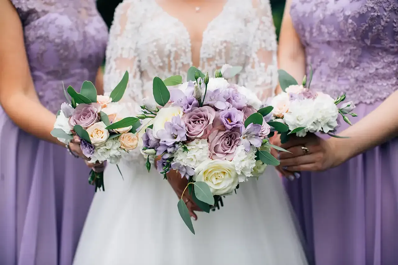 A bride and her bridesmaids are holding bouquets of purple and white flowers.
