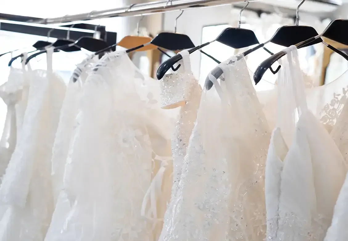 A row of white wedding dresses hanging on a rack in a store.