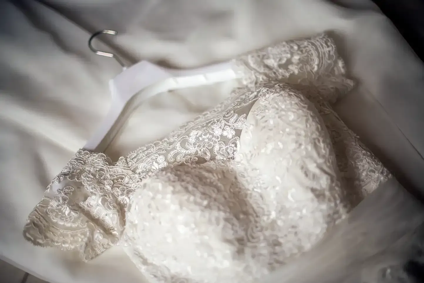 A wedding dress is hanging on a white hanger on a bed.