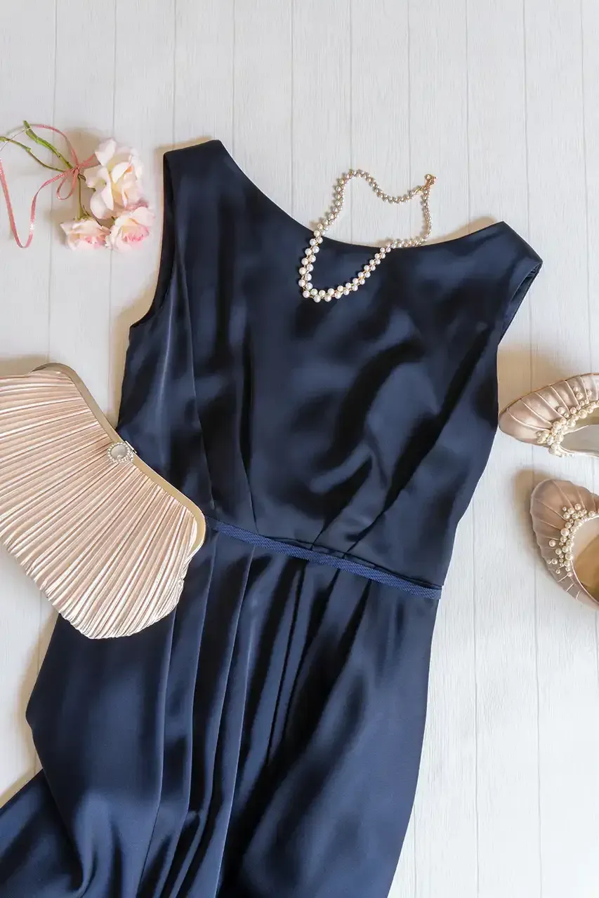 A blue dress with a pearl necklace and shoes is on a white wooden table.