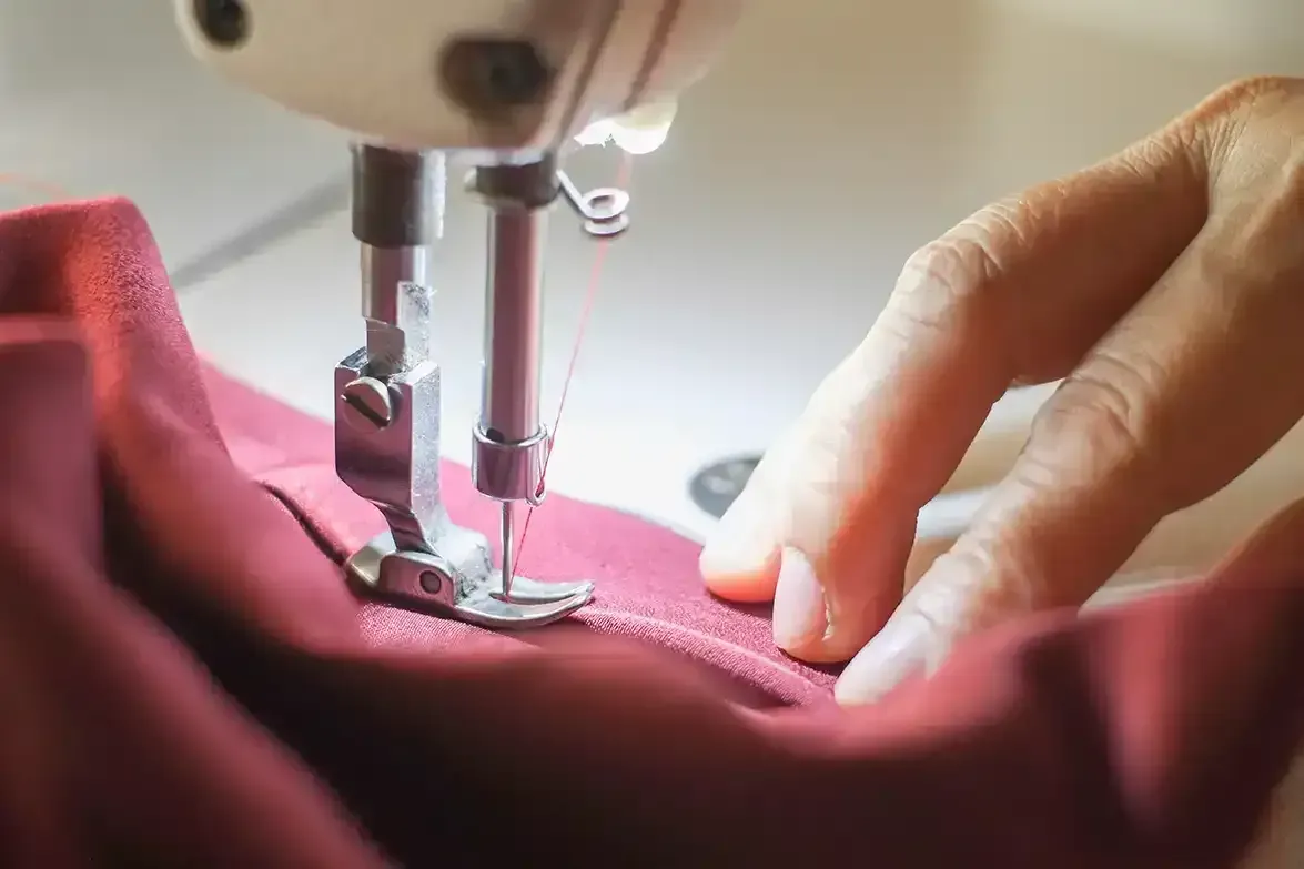 A person is using a sewing machine to sew a piece of red fabric.