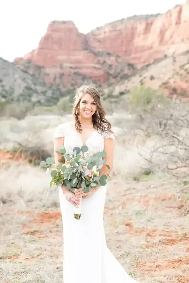 A bride in a white dress is holding a bouquet of flowers in front of a mountain.