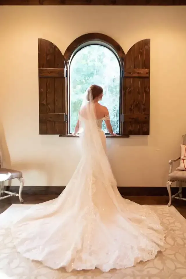 A bride in a wedding dress is standing in front of a window.