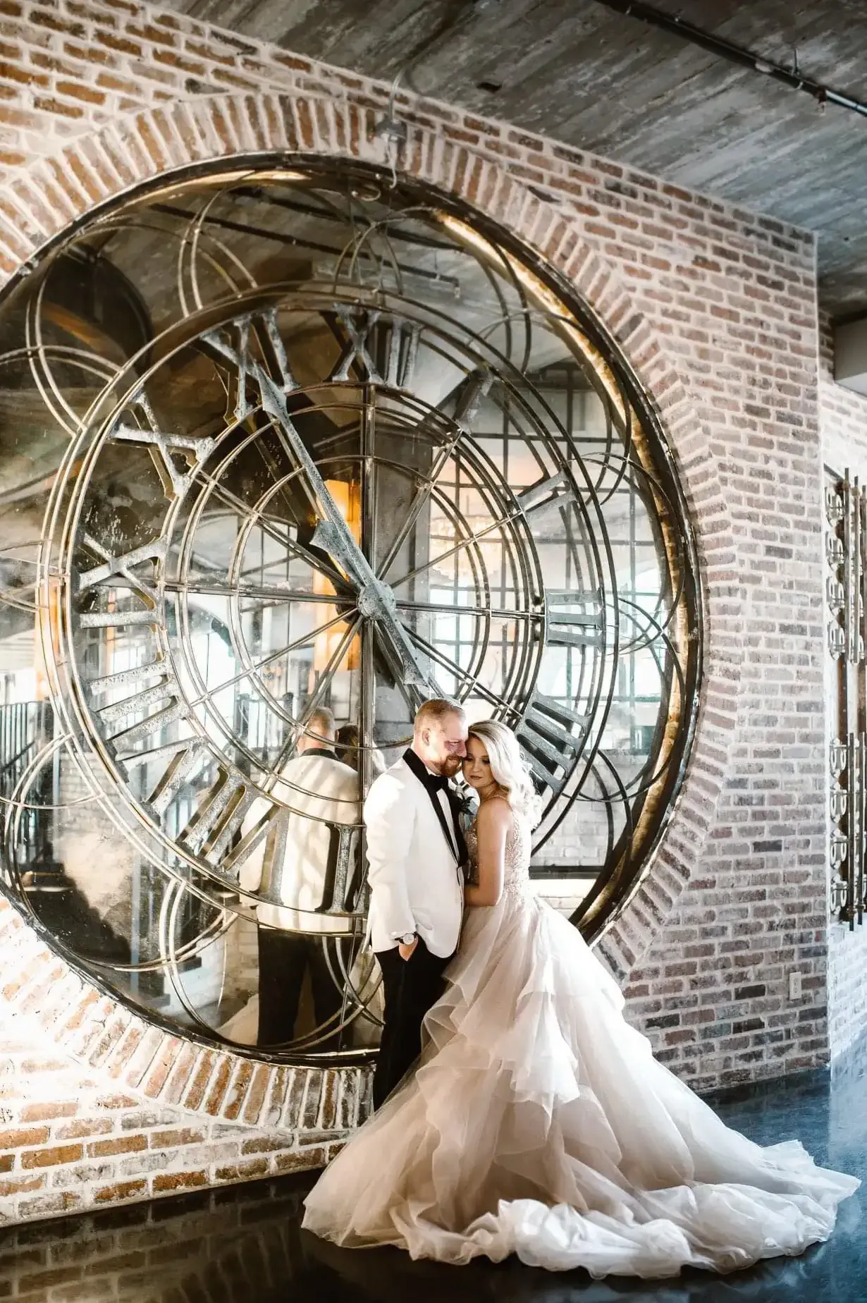 A bride and groom are posing for a picture in front of a large clock.