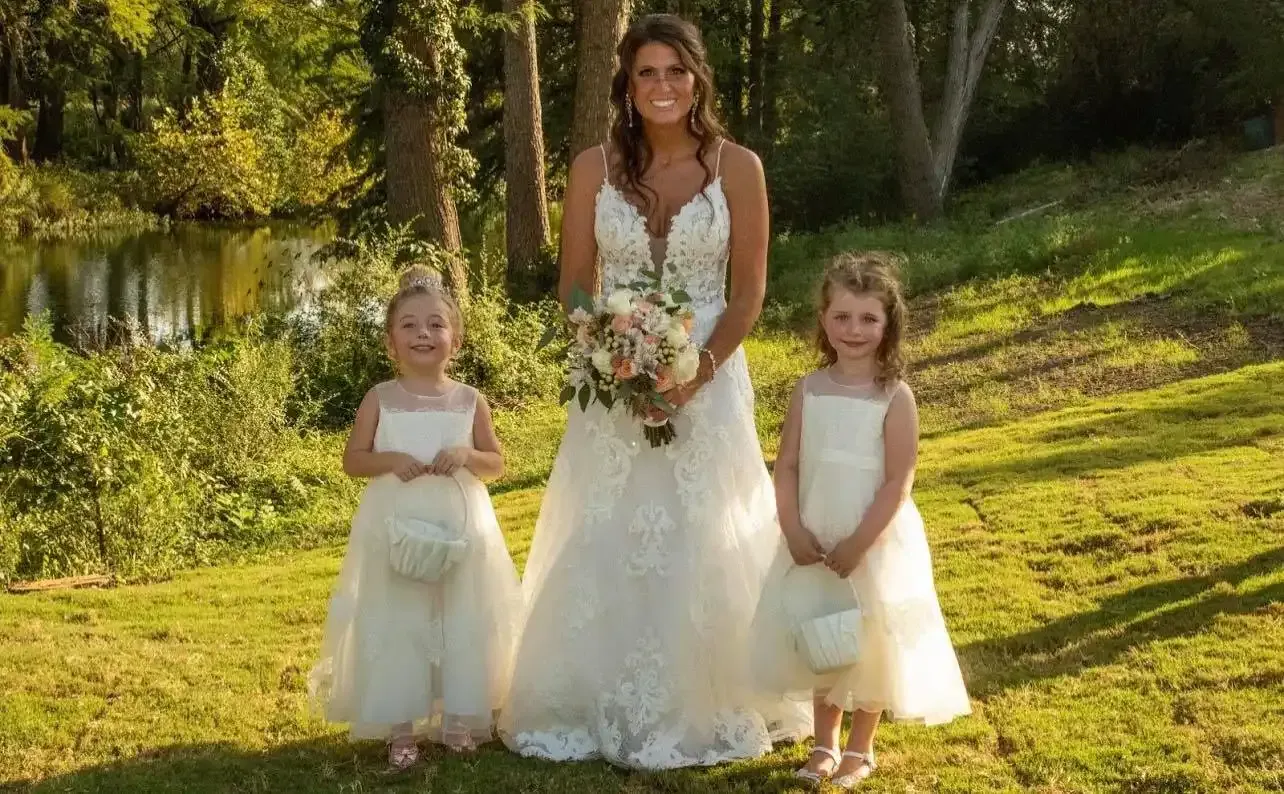 A bride and her two flower girls are posing for a picture in the grass.