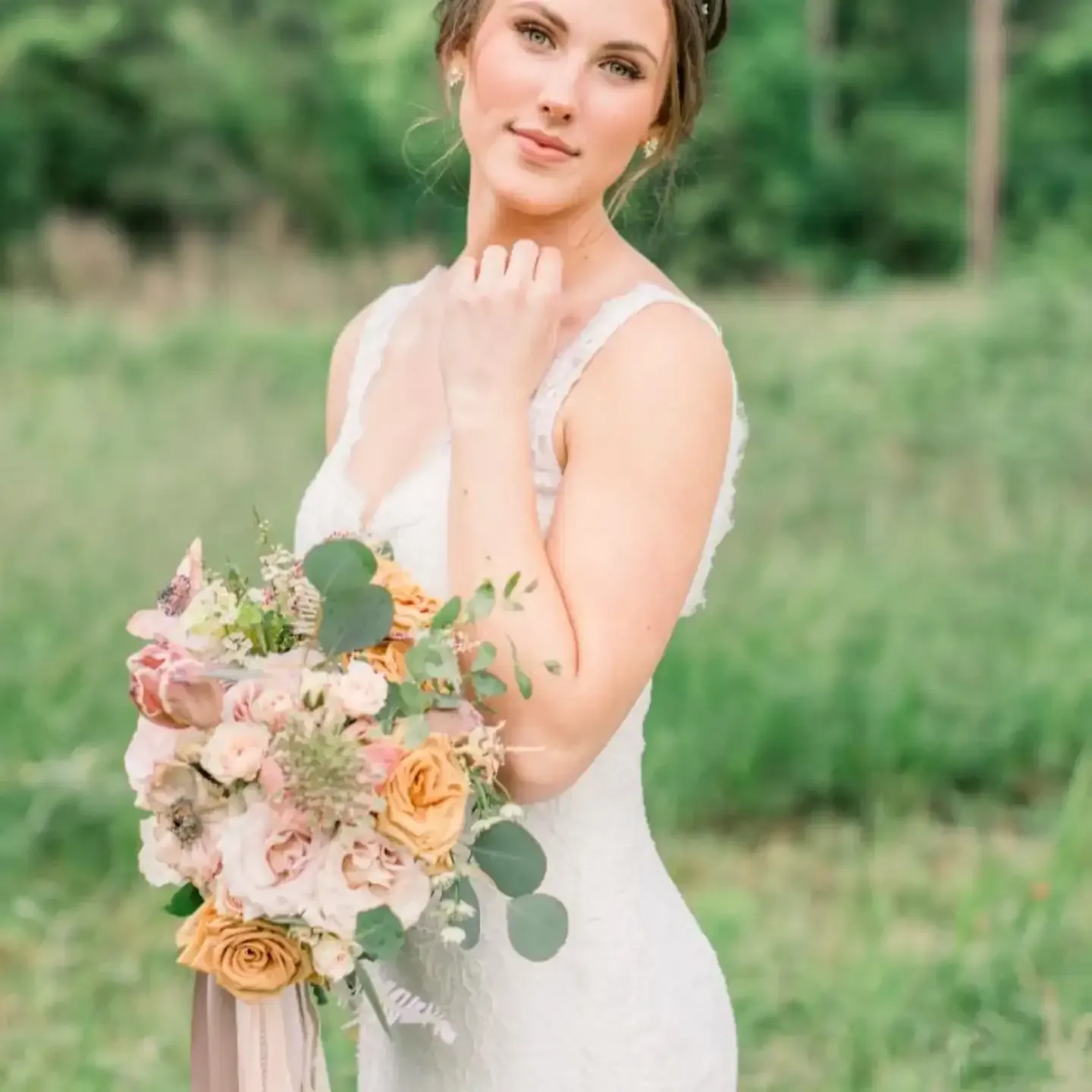 A bride in a white dress is holding a bouquet of flowers in a field.