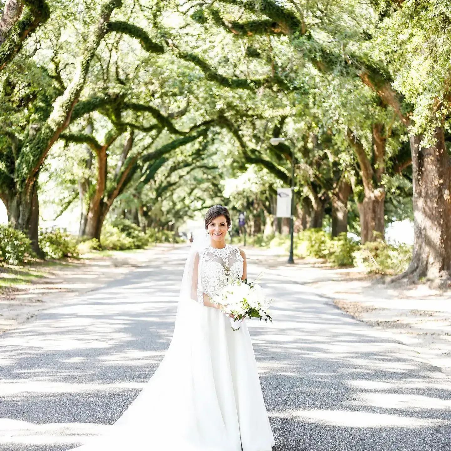 A bride in a wedding dress is standing on a road holding a bouquet of flowers.