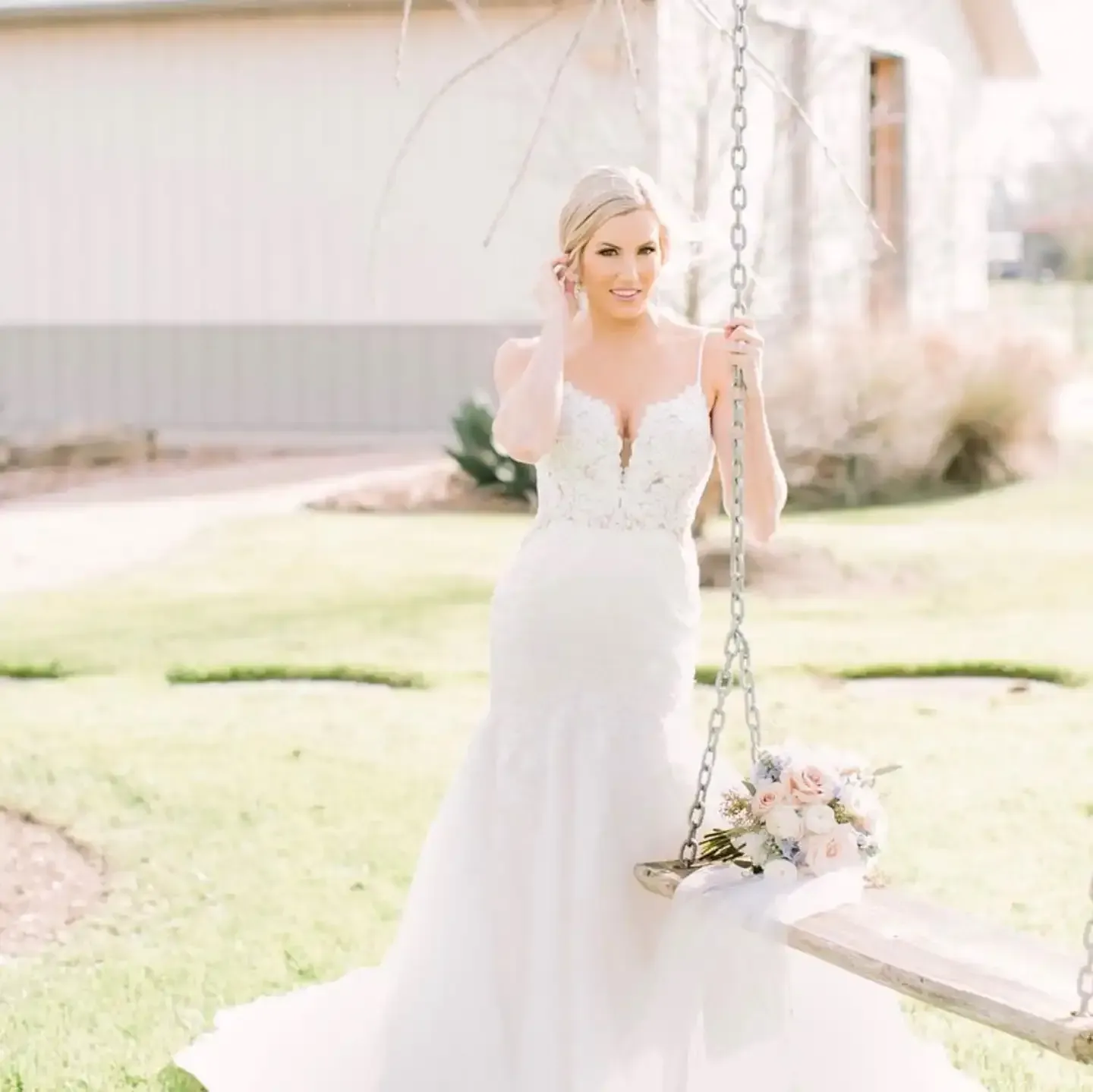 A bride in a white dress is sitting on a swing holding a bouquet of flowers.