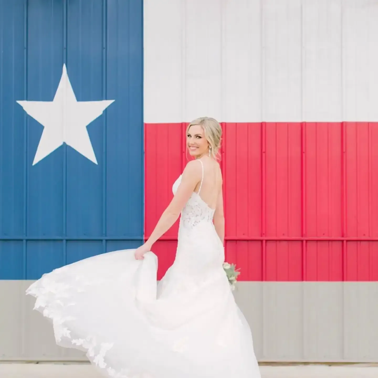 A bride in a white dress is standing in front of a texas flag.