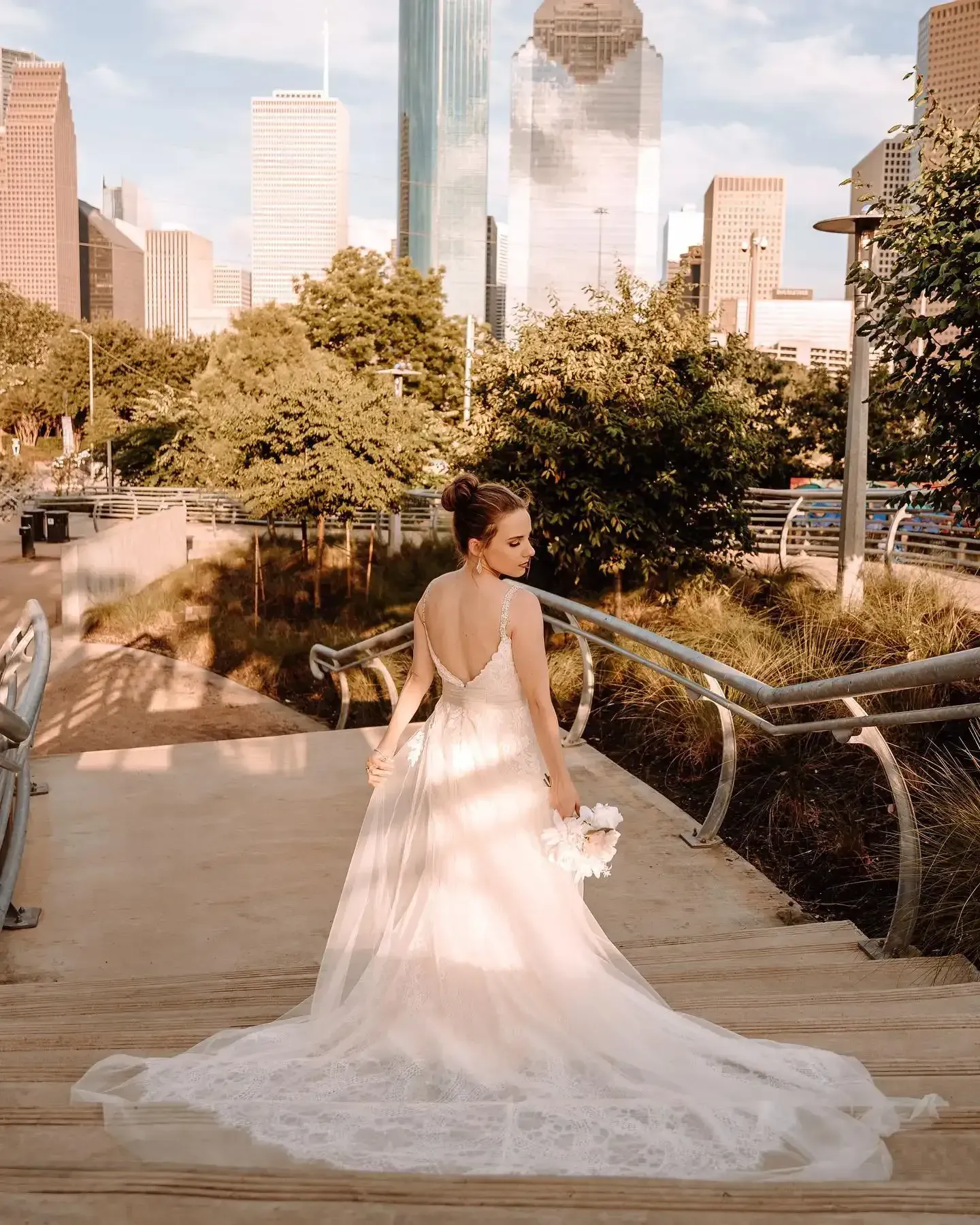 A bride in a wedding dress is standing on stairs in front of a city skyline.