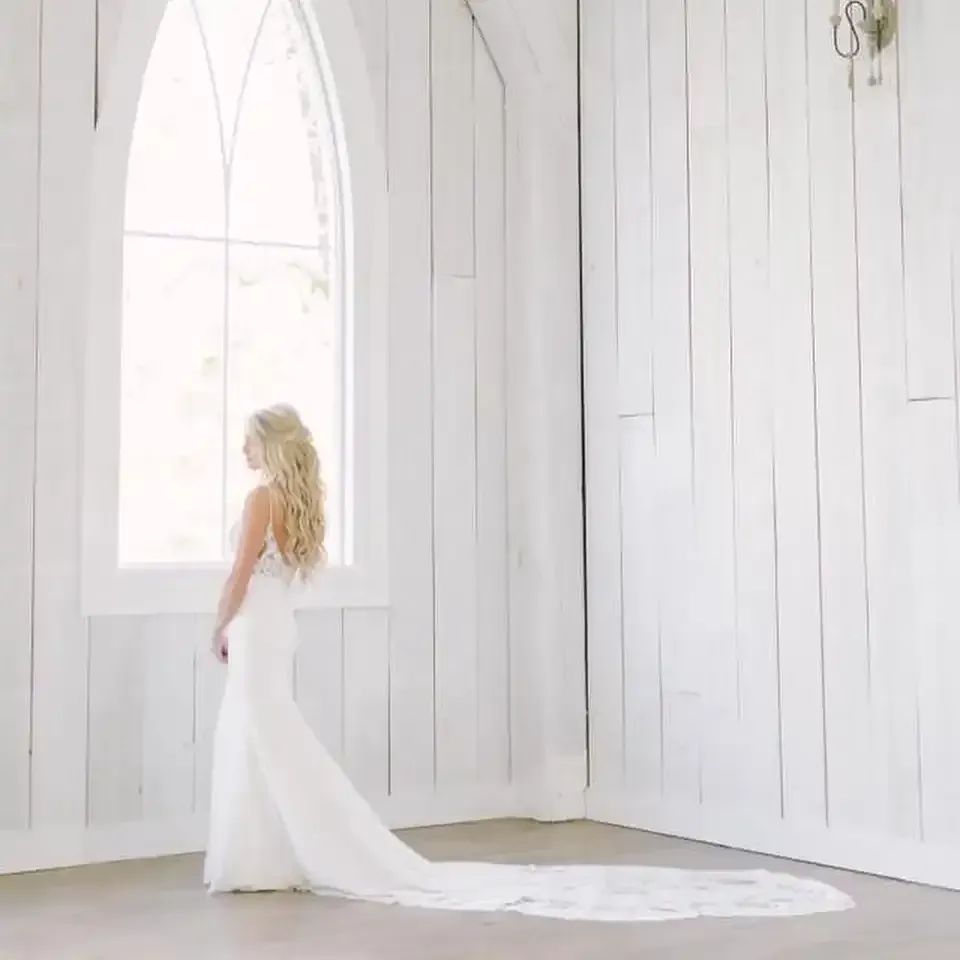 A bride in a white wedding dress is standing in front of a window.